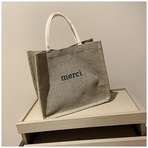 Detail showing natural jute texture and black merci print on a large tote bag