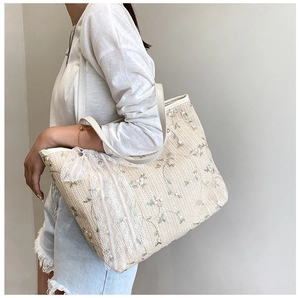 Detail of straw tote bag featuring white lace floral embroidery and leather straps