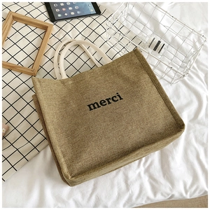 Detail of a brown linen tote bag featuring black merci lettering and woven texture