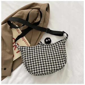 Detailed view of checkered crossbody bag featuring a plush soot sprite charm and wide strap