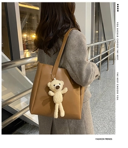 Close-up of brown soft leather tote bag with a beige plush bear pendant outdoors