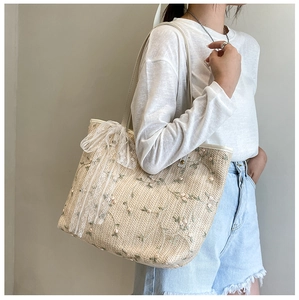 Detailed close-up of a floral embroidered straw tote bag with a white lace bow detail
