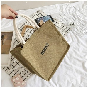 Detail of eco-friendly jute tote bag with black merci print and thick white rope handles
