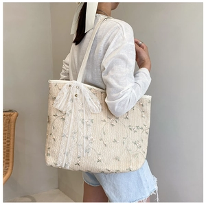 Detail showing floral embroidery and large white lace bow on the woven straw tote bag