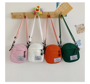 Mini canvas crossbody bags in pink, white, orange, and green hanging on a wooden hook