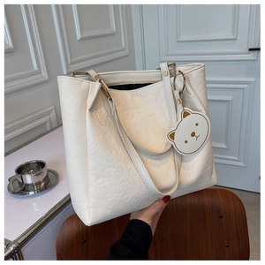 Detail of white embossed leather tote bag with teddy bear charm on a wooden chair