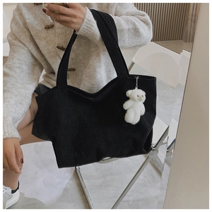 Detail of black corduroy tote bag featuring a cute white plush bear charm and long straps