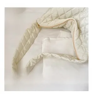 Detail of quilted wide shoulder strap on beige puffer bag with soft cotton texture