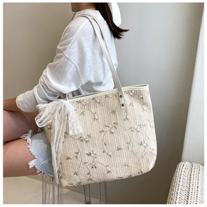 Detailed view of beige woven tote bag with pink floral embroidery and lace bow accessory
