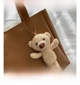 Detail of cream plush bear charm with silver bead chain on a soft tote bag