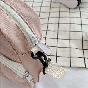 Detail of pink canvas crossbody bag showing double white zippers and black hardware