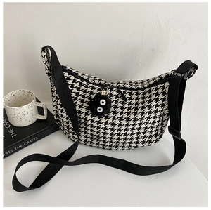 Detail of checkered crescent crossbody bag with black plush charm and adjustable strap