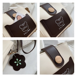 Detail of cream crossbody bucket bag with bear motif pocket and wooden button closure