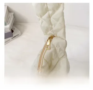 Detailed close-up of smooth gold zipper on white quilted padded nylon shoulder bag