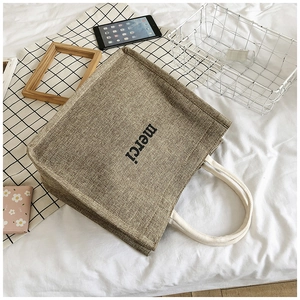 Close-up of a rustic linen tote bag with merci print and soft white cotton rope handles