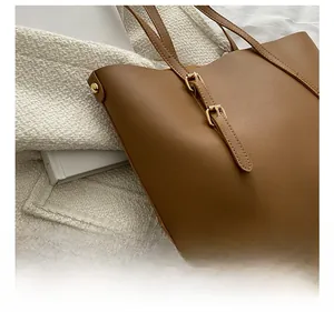 Detailed close-up of textured caramel leather tote bag with gold hardware buckle