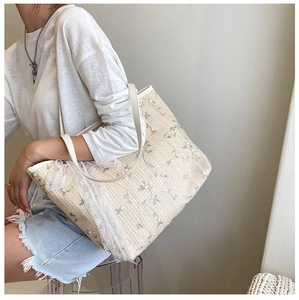 Detail of a cream straw tote bag featuring floral embroidery and delicate lace trim