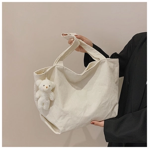 Close-up of cream corduroy tote bag with plush bear charm and striped texture detail