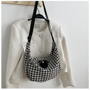 Detail of houndstooth hobo bag featuring a black pom-pom charm and adjustable strap