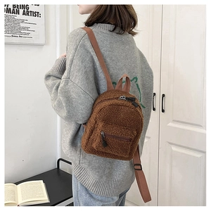 Detailed back view of a mini brown teddy fleece backpack worn by a model in a cozy room