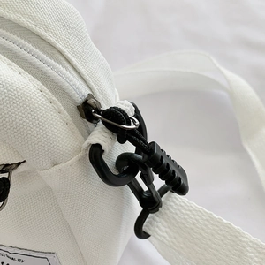 Side view of white canvas crossbody bag with black zipper hook and strap detail