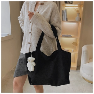 Detail of black corduroy tote bag with dual straps and cute white teddy bear charm