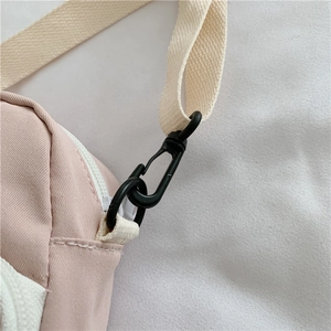 Detail of pink canvas crossbody bag showing white zipper and removable beige shoulder strap