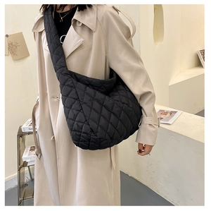 Detail of black quilted cloud bag with wide shoulder strap worn over a beige trench coat
