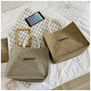 Detail of linen tote bags with merci print and woven handles in a lifestyle setting