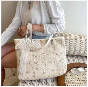 Detail of floral embroidery on straw tote bag with white lace bow and leather handle