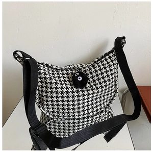 Detail of checkered crossbody bag with black soot sprite plush pendant and wide strap