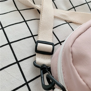 Detail of light pink crossbody bag with cream woven strap and black plastic hardware
