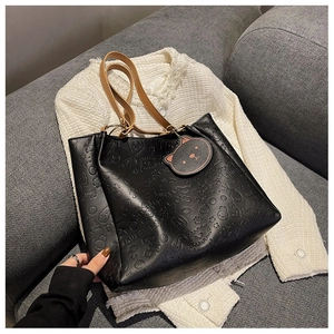 Detail of black embossed tote bag with cartoon patterns and cute bear charm pendant