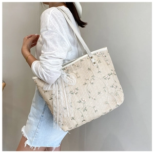 Detail of floral embroidery and white lace bow on a woven straw tote bag surface