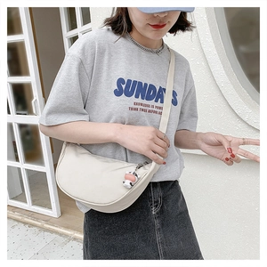 Close-up of cream nylon crescent bag with cow charm and wide shoulder strap