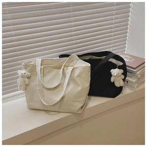Detail of corduroy tote bags in cream and black with a cute plush bear charm