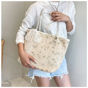 Detail of straw tote bag featuring floral embroidery and a large white lace bow accent
