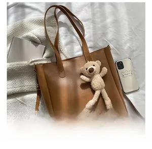 Detail view of large brown faux leather tote bag with shoulder straps and plush bear charm