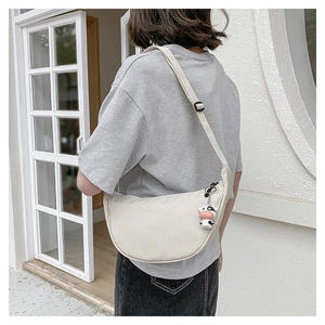 Detailed side view of off-white nylon crescent crossbody bag with cow charm on model