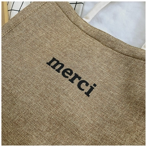 Detailed close-up of textured burlap fabric and black merci print on large tote bag