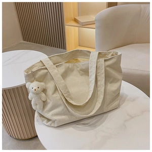 Detail of cream corduroy tote bag texture with cute plush bear charm on a marble table