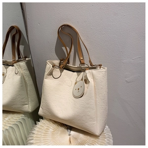 Detail of embossed cartoon patterns on cream tote bag with brown leather shoulder straps