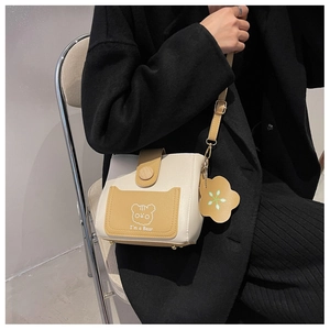 Detail of a contrast color bucket bag with cartoon bear print and floral pendant accessory