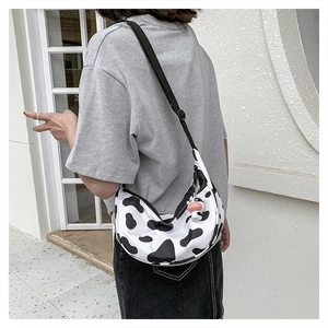 Close-up of cow print crossbody bag with cute calf doll charm and adjustable strap