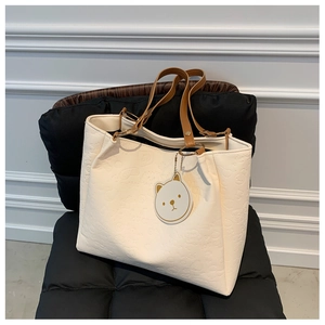 Close-up of embossed cream tote bag with brown leather straps and a cute bear charm