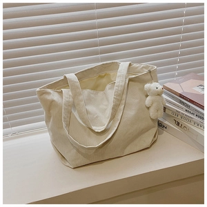 Detail of cream corduroy tote bag with plush bear charm and sturdy top zipper closure