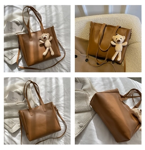 Detail view of a brown leather tote bag with a soft plush bear charm and adjustable strap