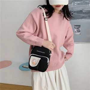 Detail of black canvas crossbody bag featuring pink bear patch and white adjustable strap