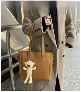 Brown leather tote bag with cute bear pendant shown on model in gray winter coat