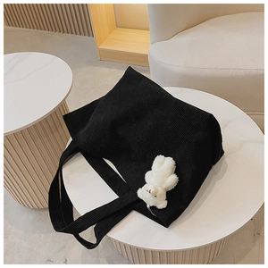 Detail of black corduroy tote bag featuring a cute white teddy bear plush charm